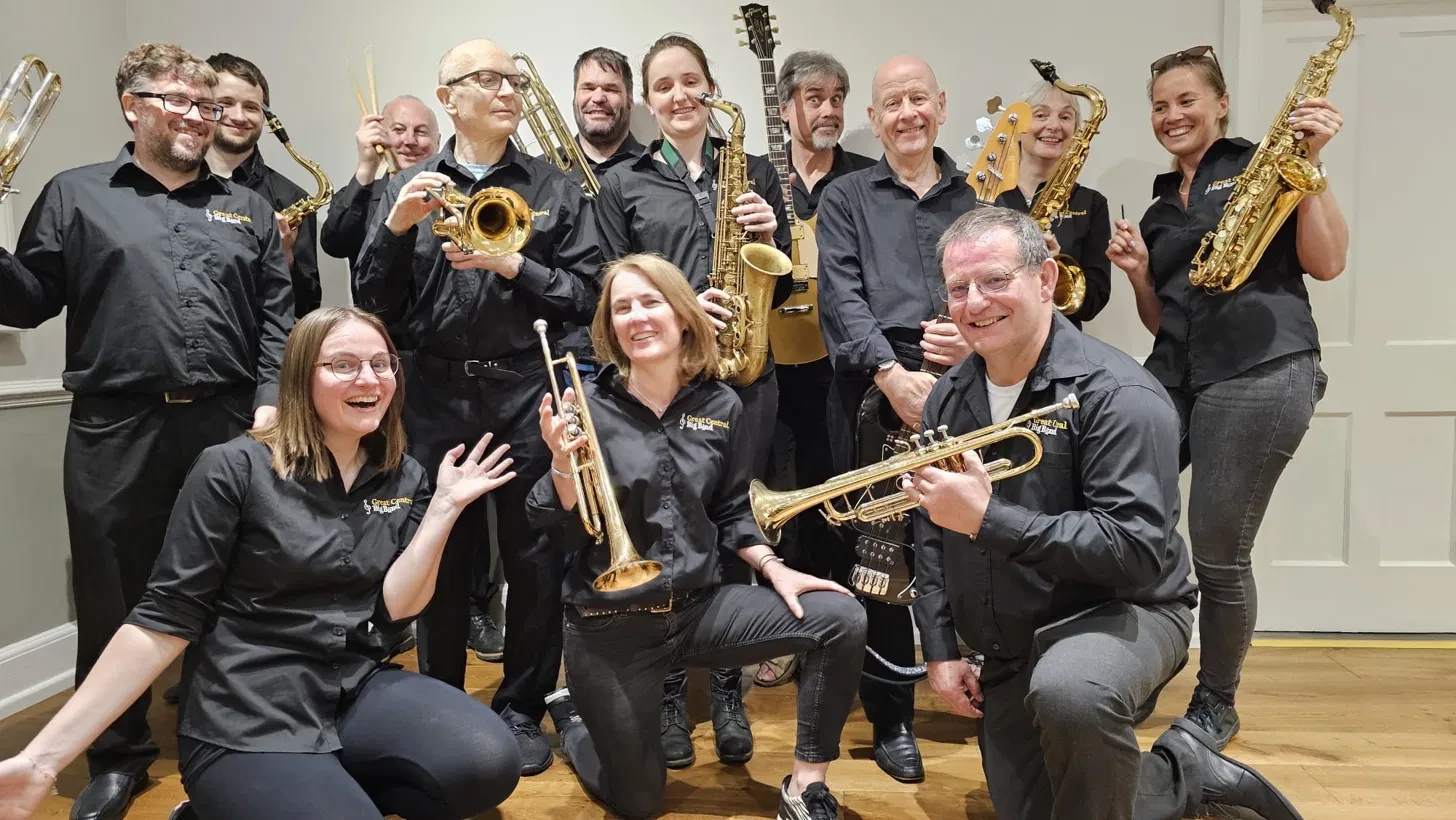 The band in their black Great Central Big Band shirts, grinning and holding up saxophones, trumpets, trombones, guitars and drumsticks